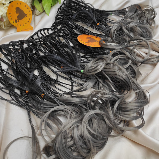 Collection of black and gray hair extensions on a white fabric background with decorative elements.