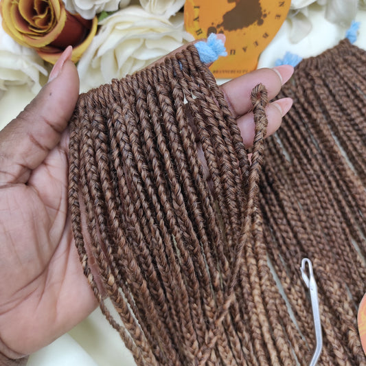 Brown braided hair extensions held by a hand with a decorative background