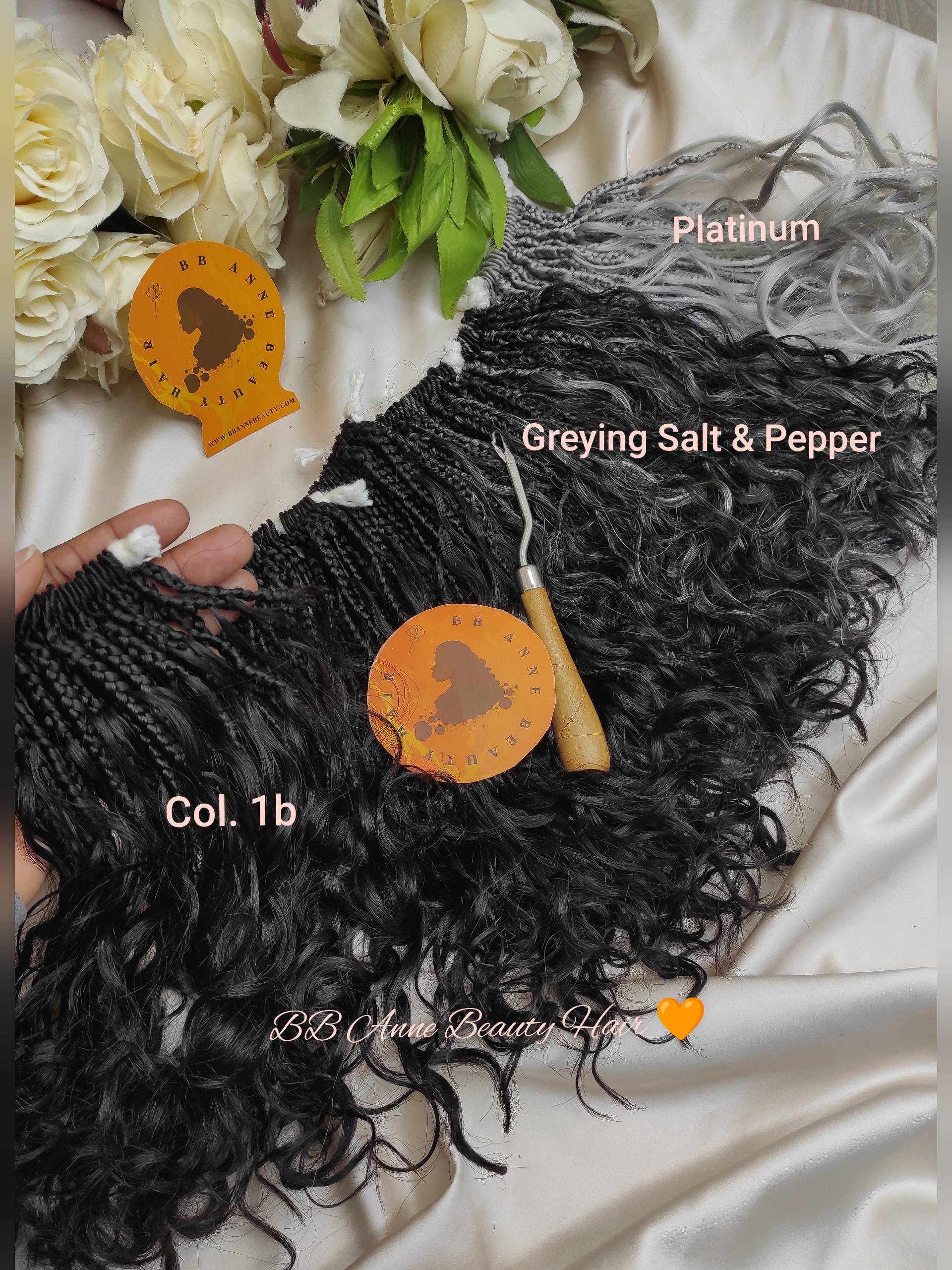 Black curly hair extensions with color options labeled on a white surface with flowers.