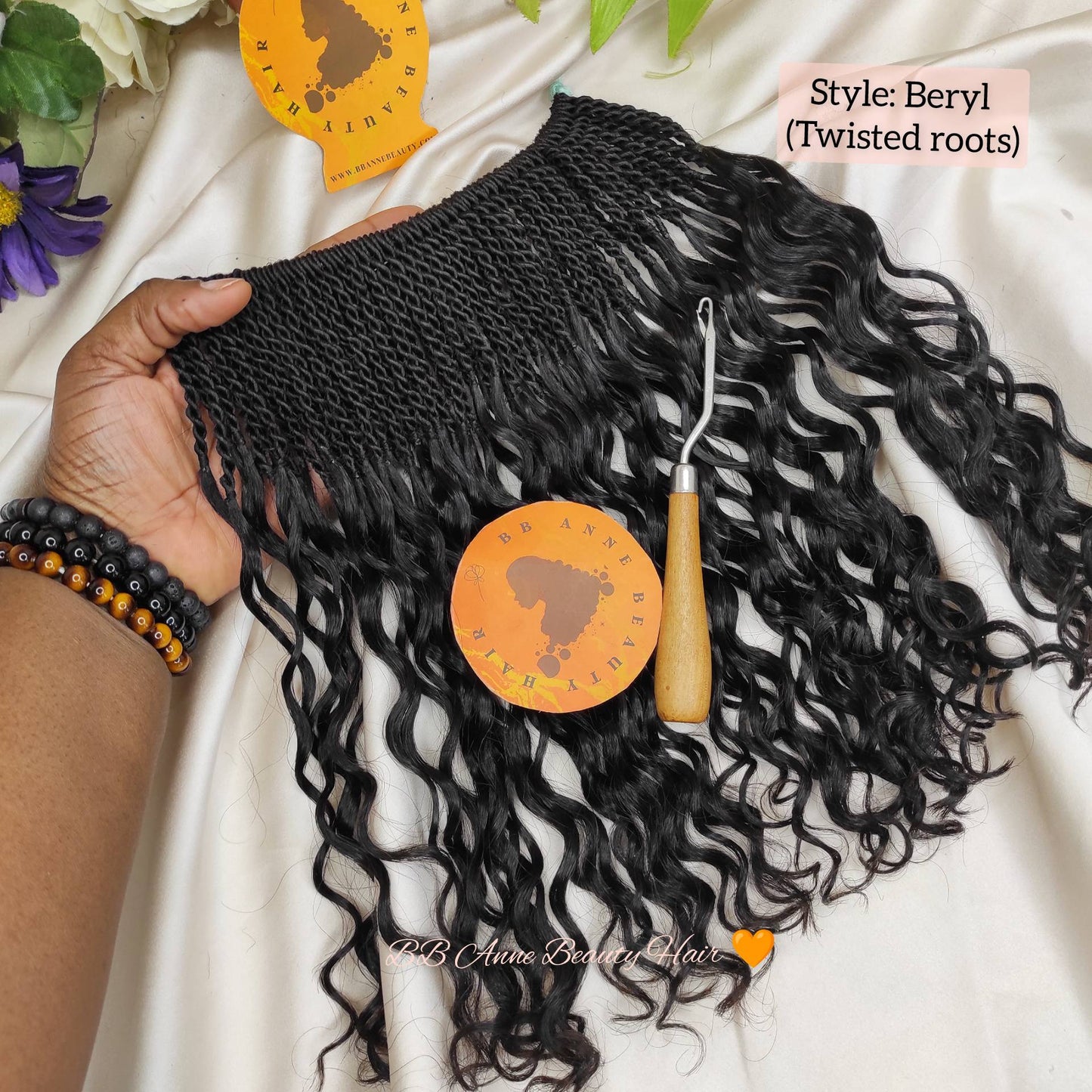 Black curly human hair extension held by a hand with a white background and bb anne beauty brand logo. 