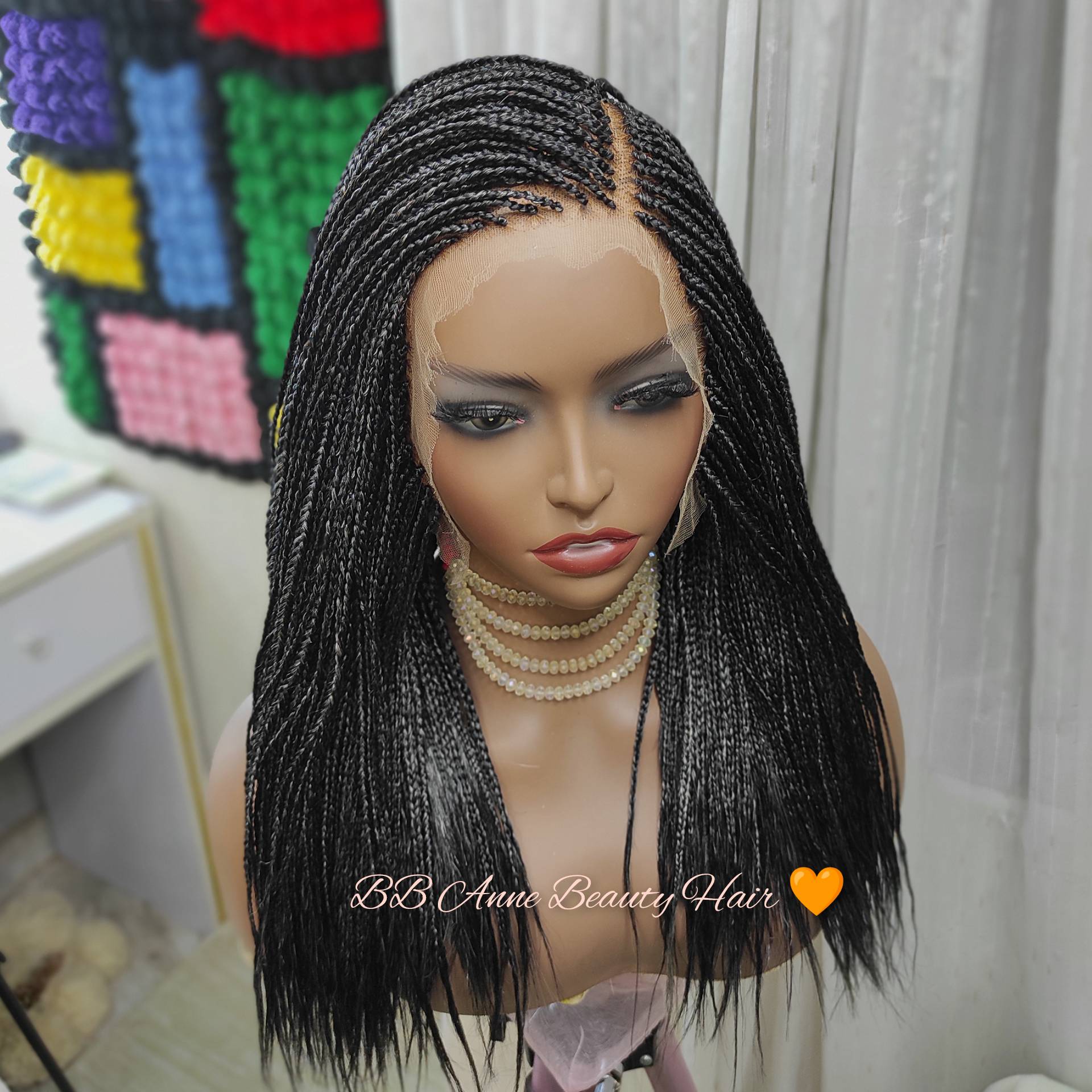 Mannequin head with a black braided wig in front of a colorful geometric pattern.