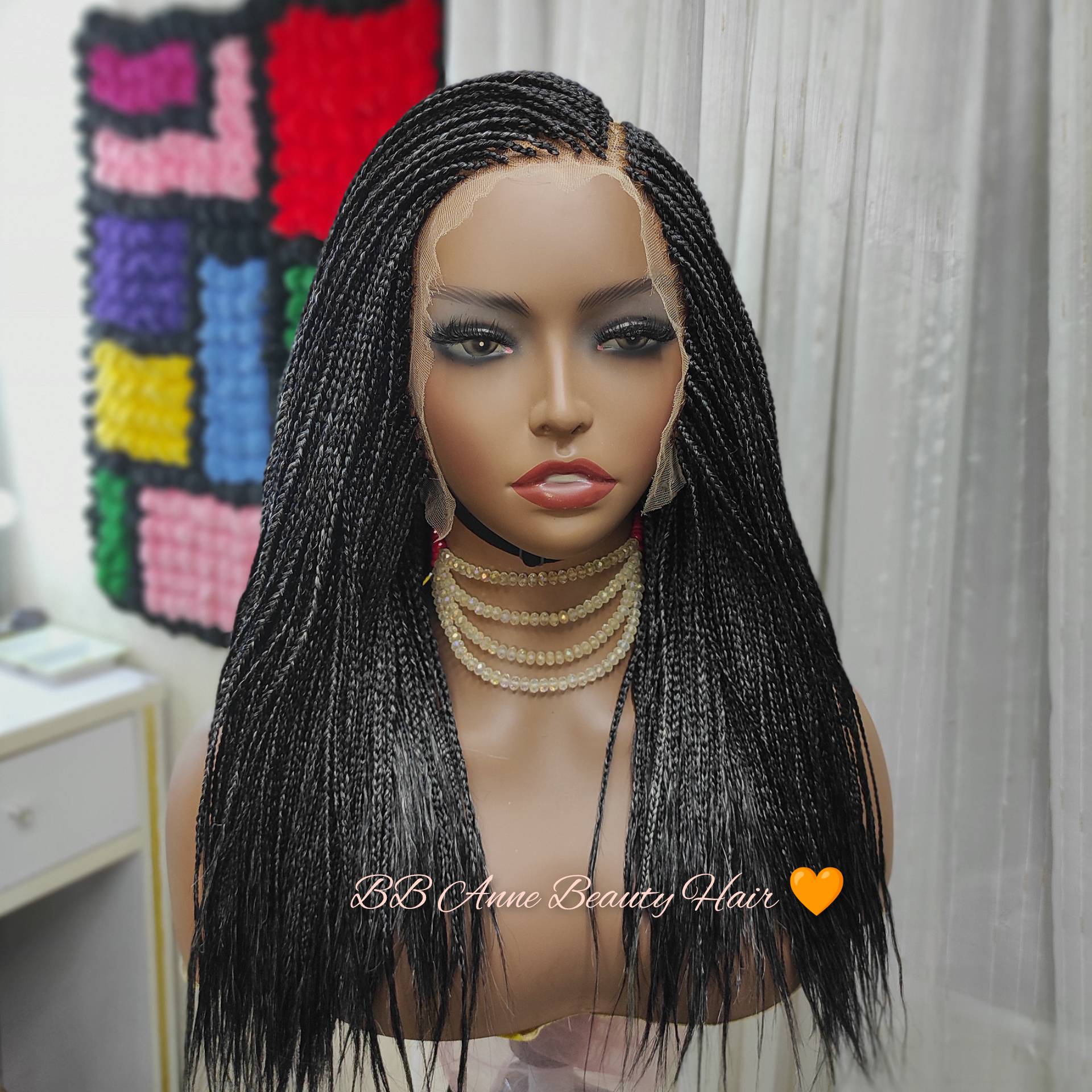 Mannequin head with a black braided wig in front of a colorful quilt.