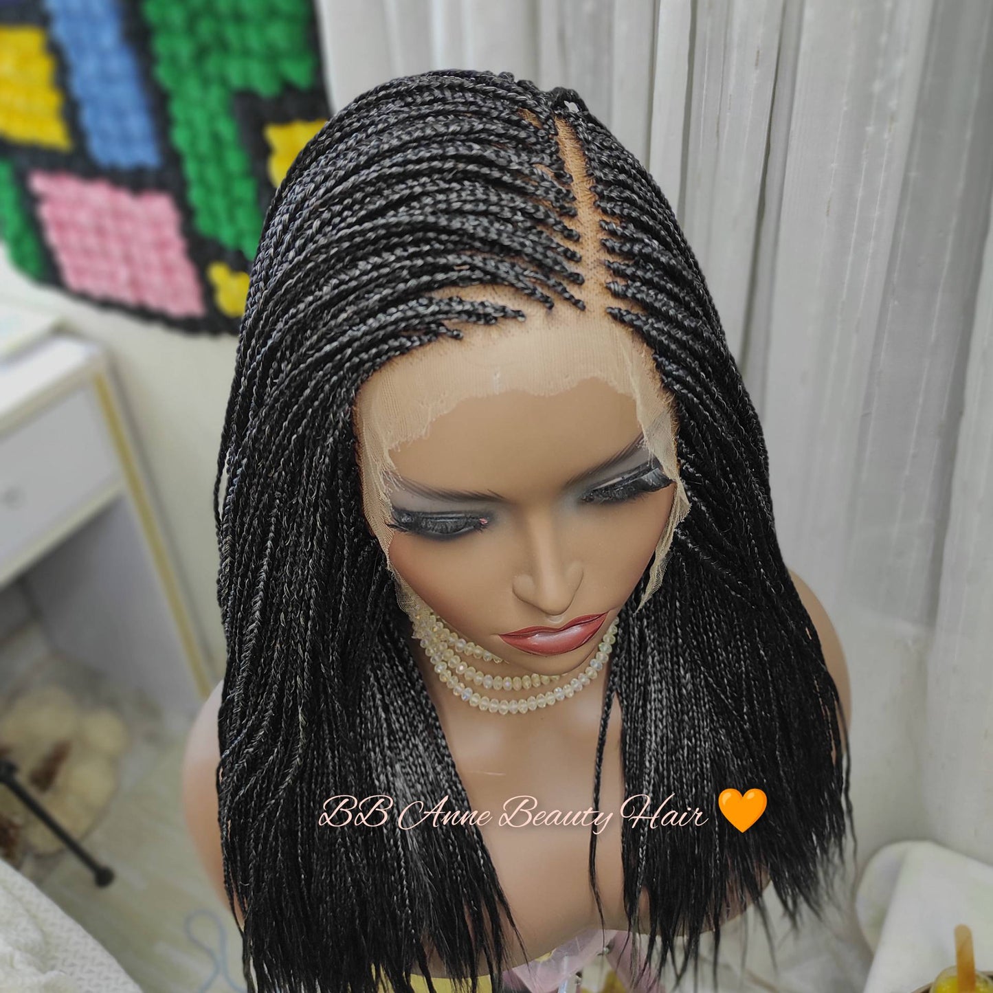 Mannequin head with a black braided wig in a room with colorful wall art.