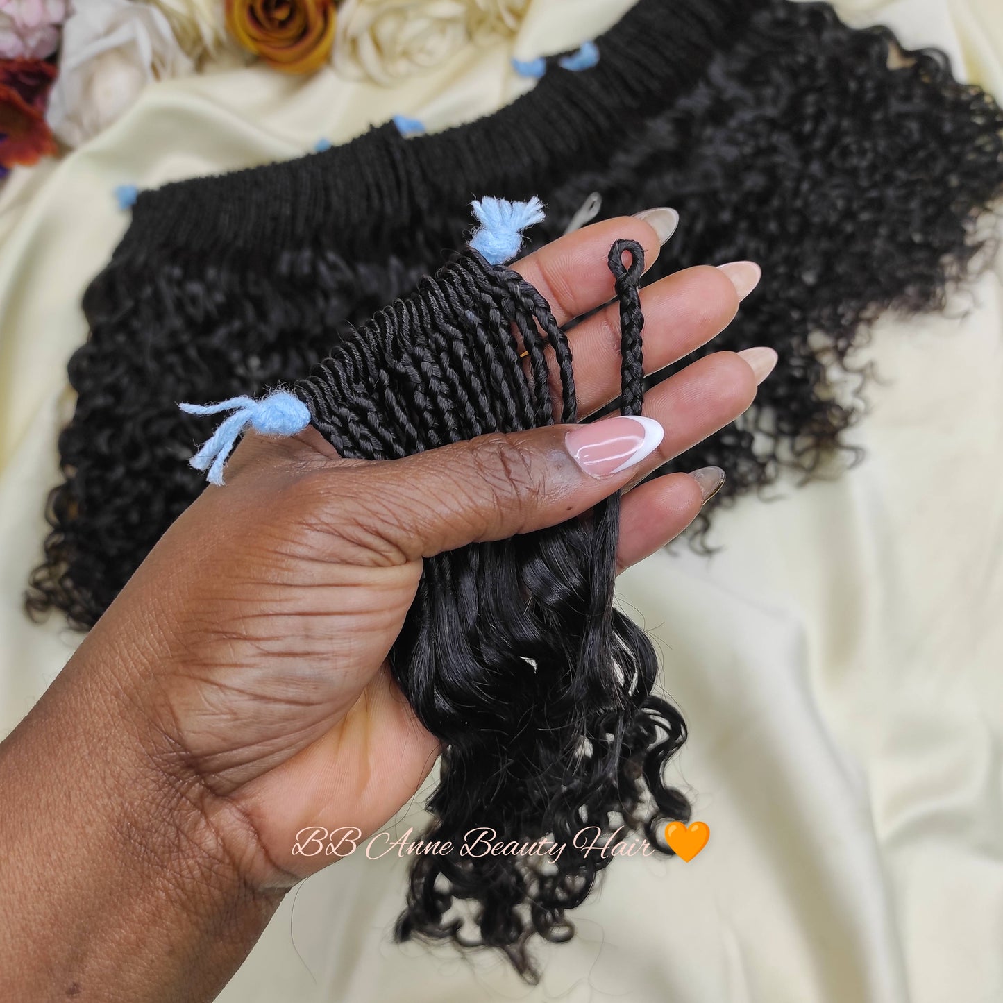 Hand holding a section of curly hair extensions with a blurred floral background