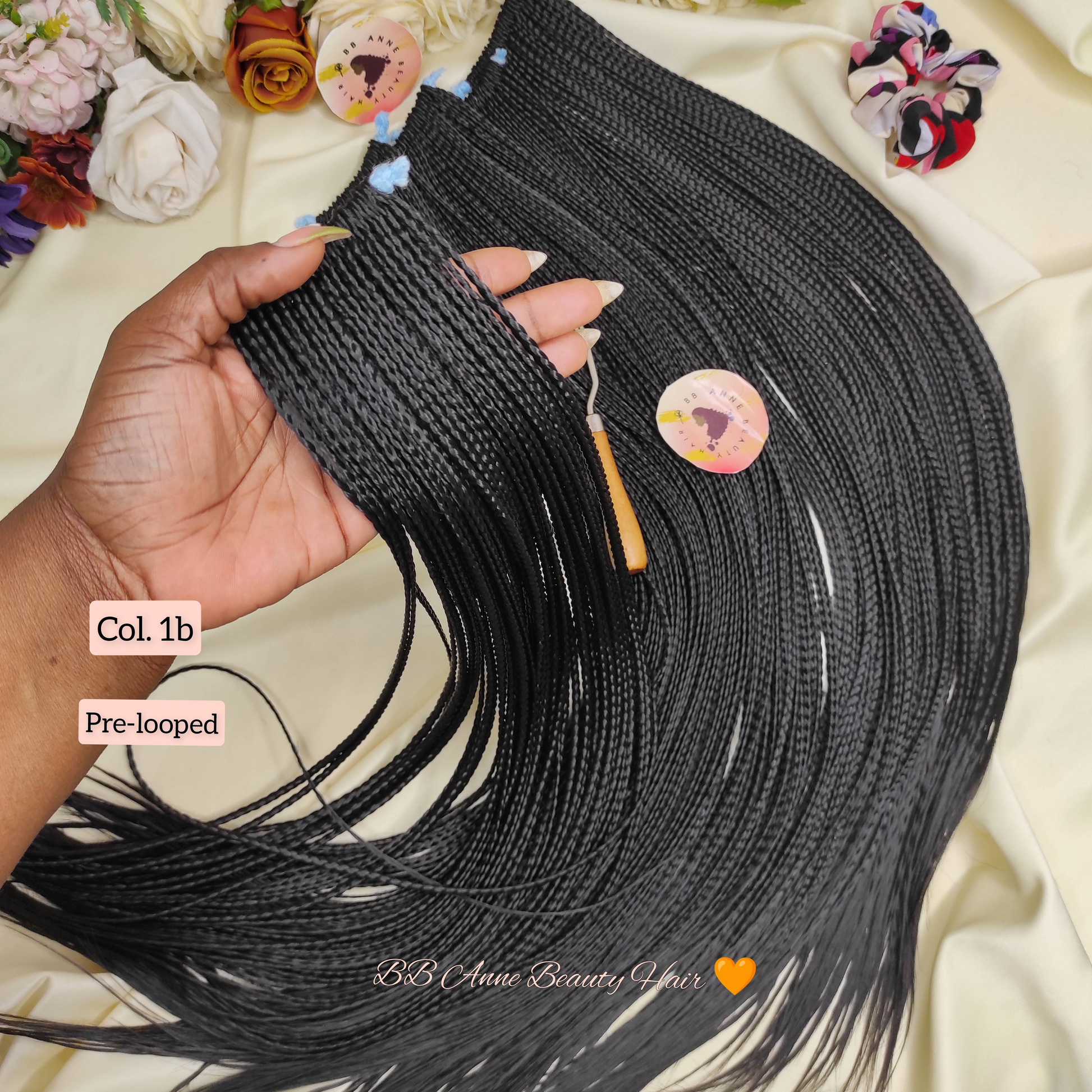 Black microbraids held by a hand with decorative elements and text overlay on a floral background.