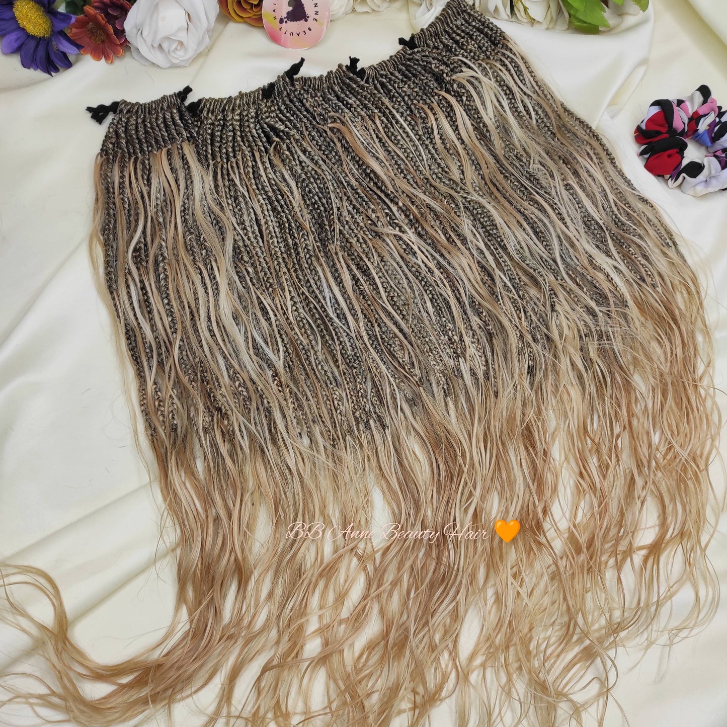 Blonde and brown braided hair extensions on a white surface with colorful flowers in the background.