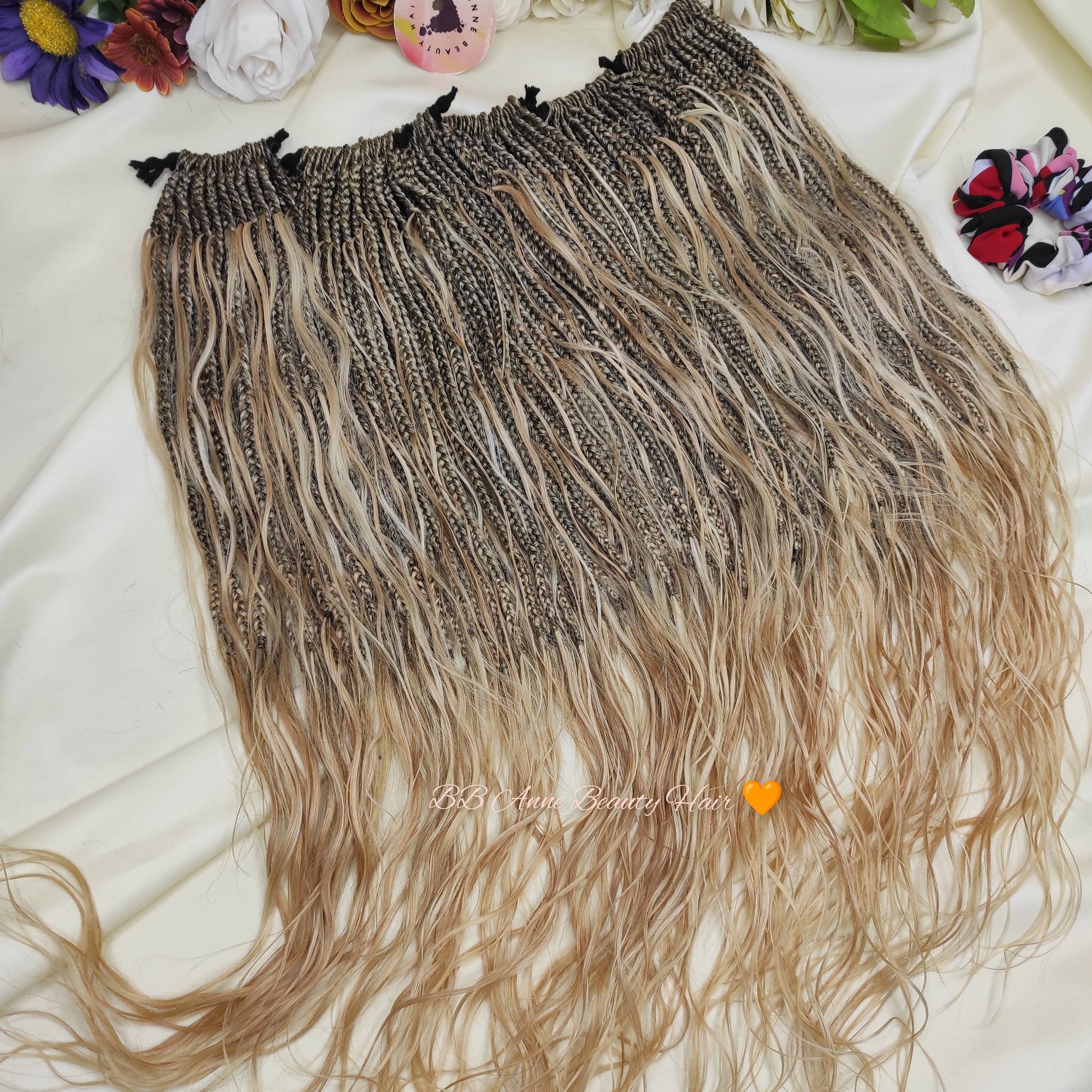 Blonde and brown braided hair extensions on a white surface with colorful flowers in the background.