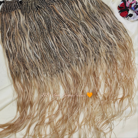 Blonde and brown braided hair extensions on a white surface with colorful flowers in the background.