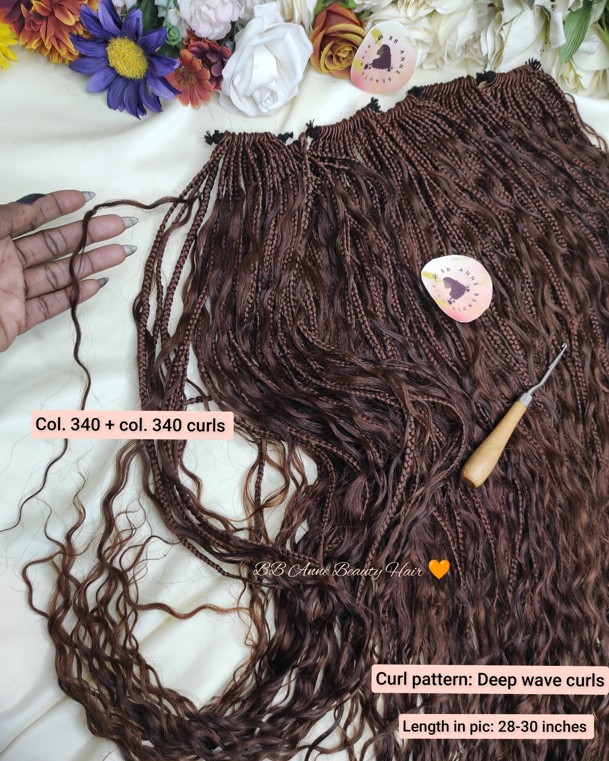 Brown braided hair extensions with a crochet hook on a white surface with flowers.