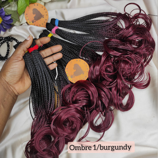 Ombre braided hair extensions in black to burgundy color with a hand holding them, on a white background.