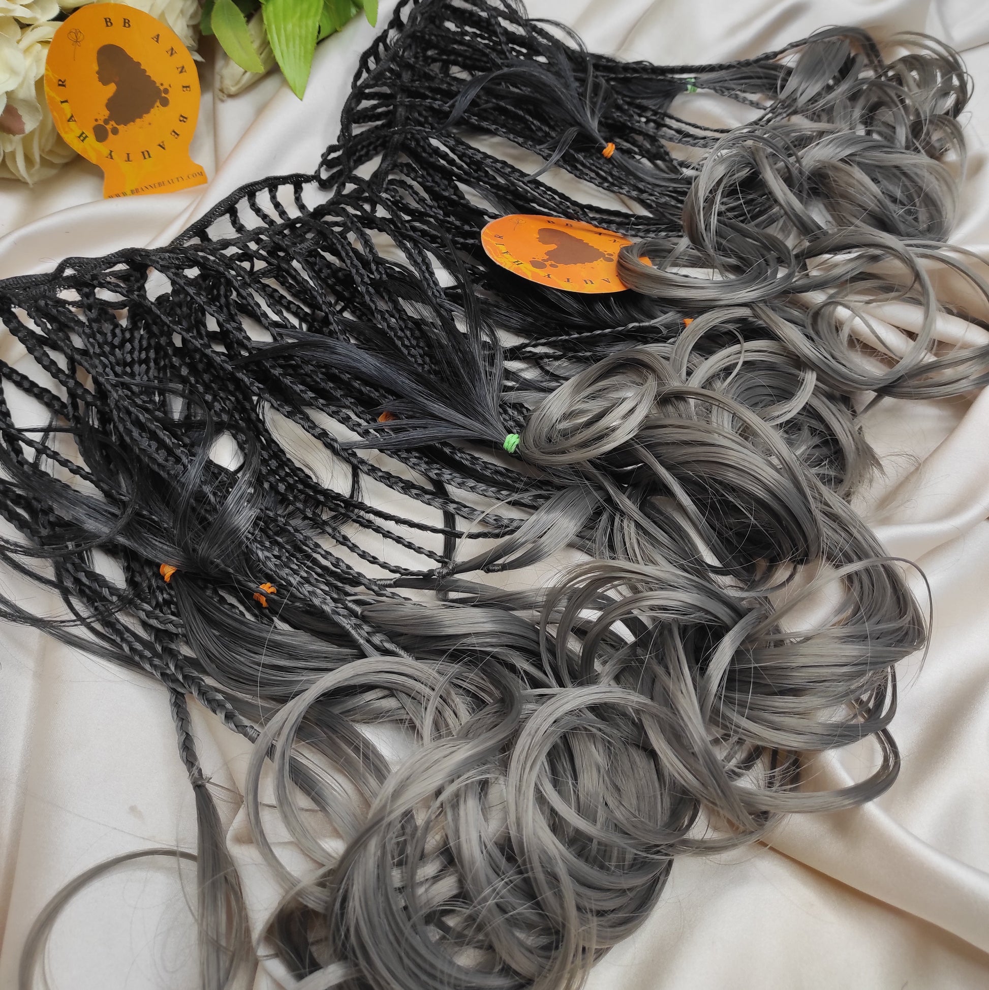 Collection of black and gray hair extensions on a white fabric background with decorative elements.