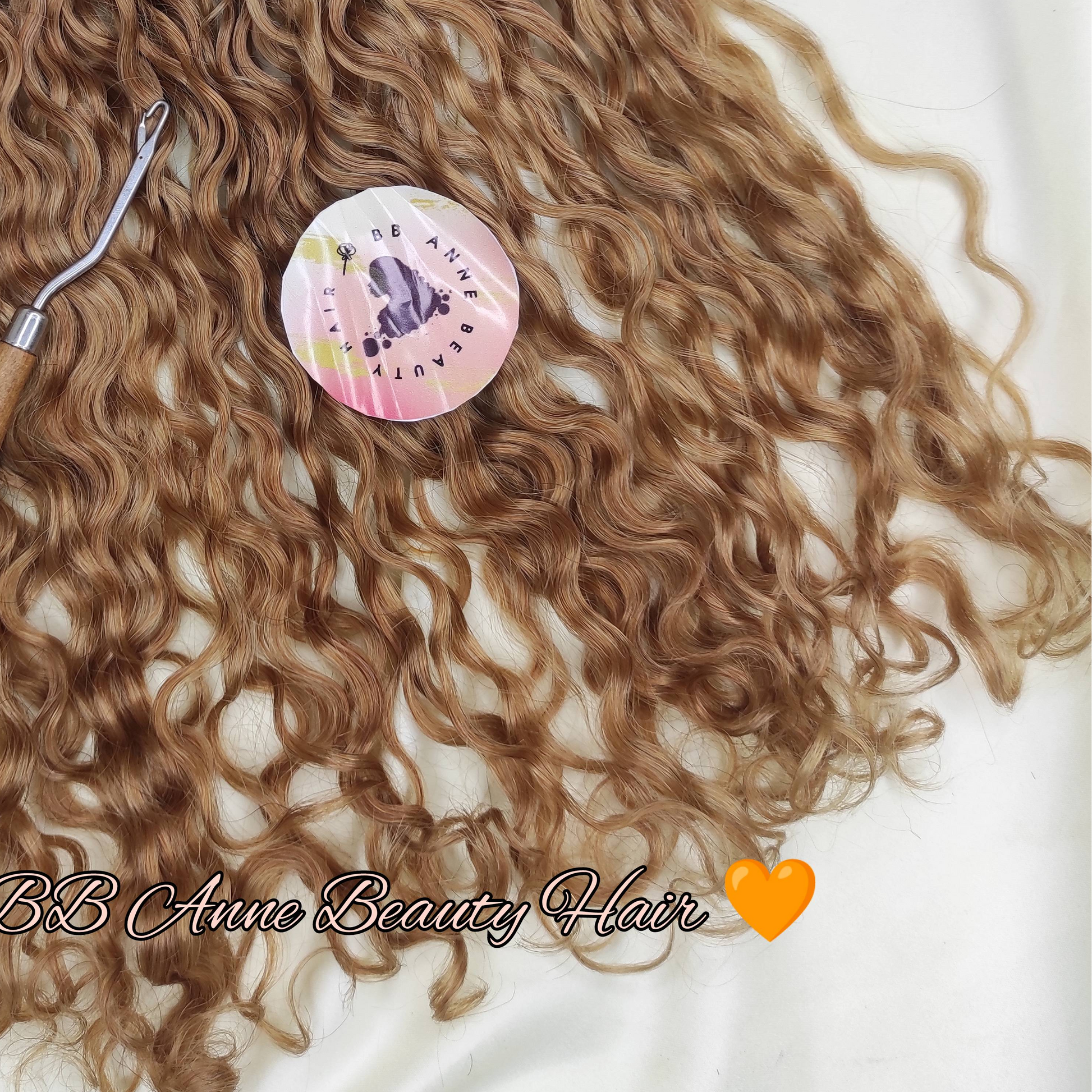 A bundle of pre-braided human hair crochet braids in a honey blonde shade, labeled 'AMARA' and 'Color 27 (Honey Blonde)', displayed on a white fabric background with a styling tool and decorative flowers.